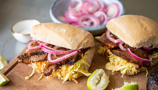 two ciabatta rolls on board with onion, slaw and beef inside