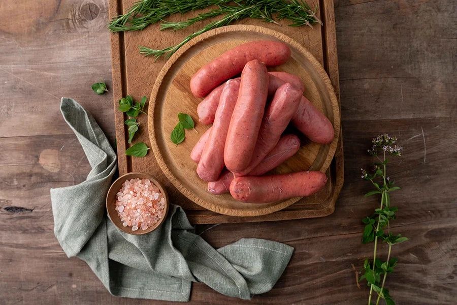 board with raw sausages on it and small bowl of pink salt