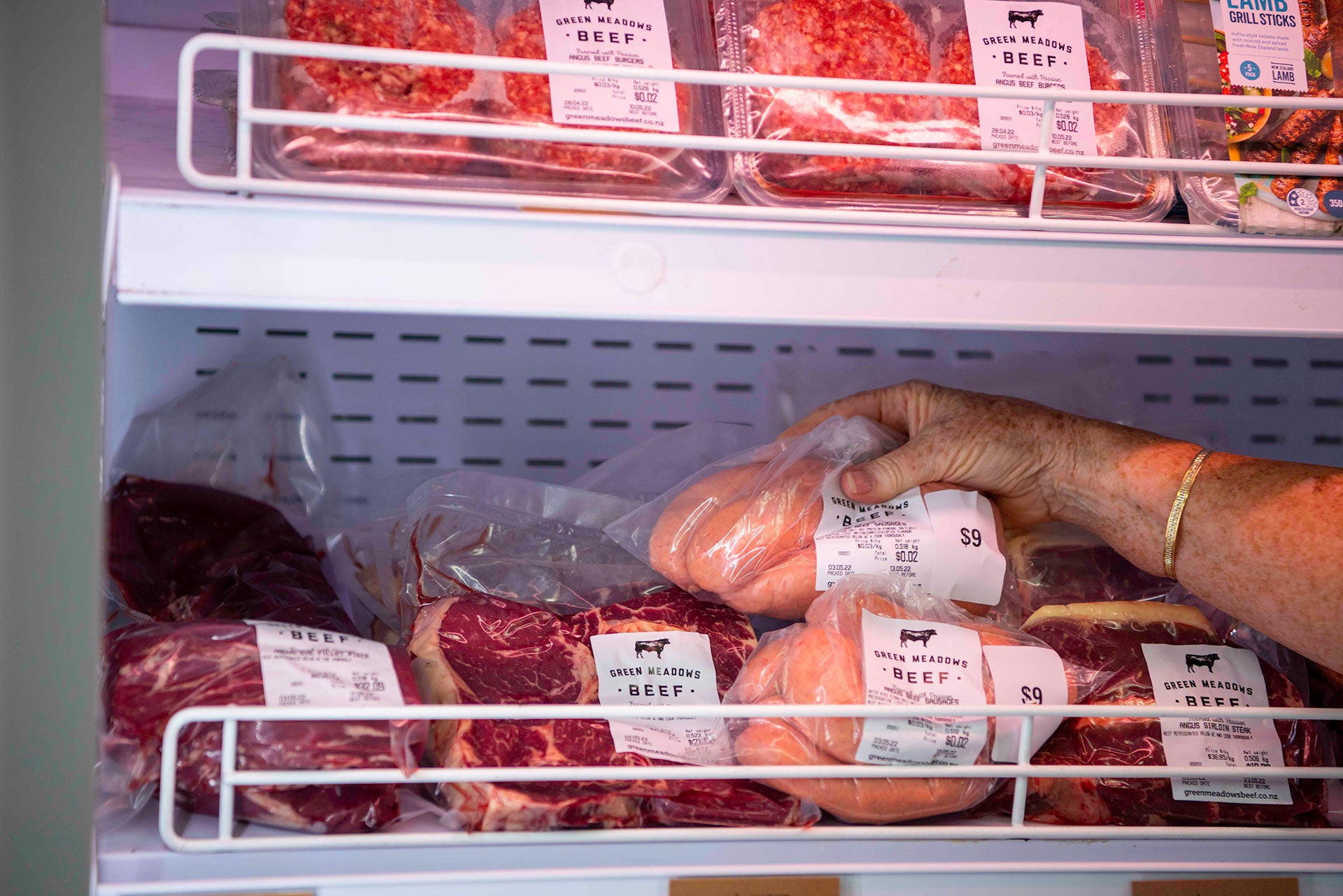 Hand grabbing angus beef sausages from shelf of meat