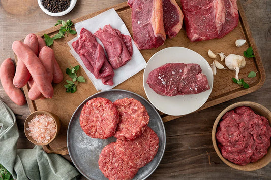 Variety of beef plated and on chopping boards with garlic, herbs, pepper and salt