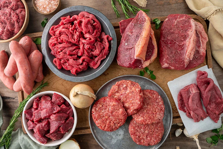 Raw beef cuts laid out on kitchen table with herbs