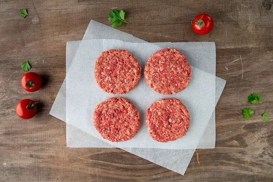 Four patties sitting on baking paper with mini tomatoes and herbs