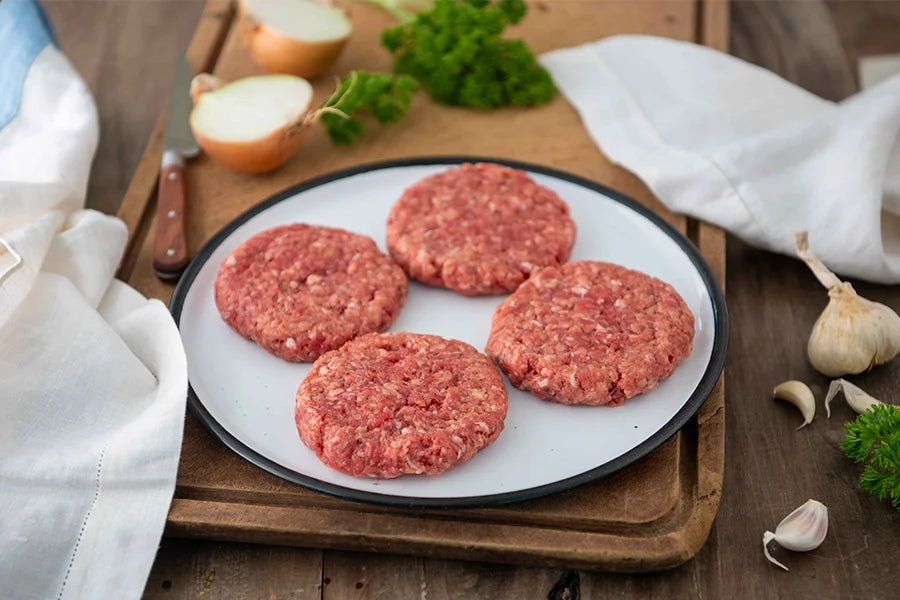 4 beef patties on a white plate, on top of a chopping board