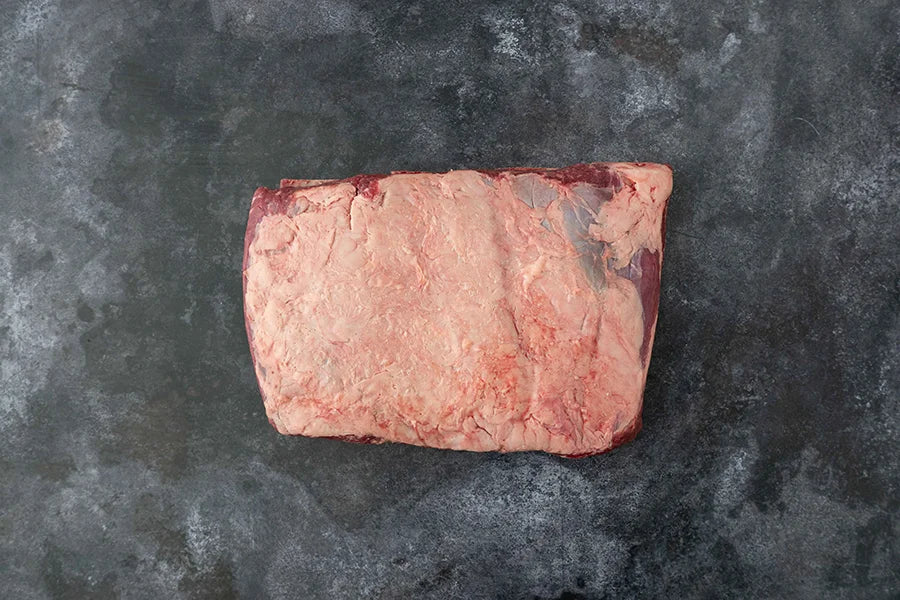 Piece of Beef brisket, fat side up - sitting on dark marble kitchen table