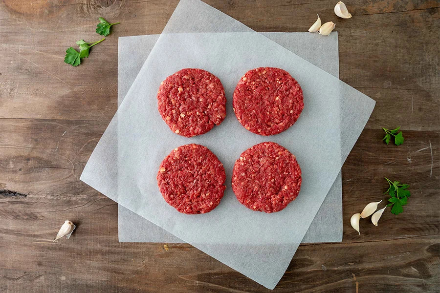 4 patties on baking paper with garlic cloves and coriander around it