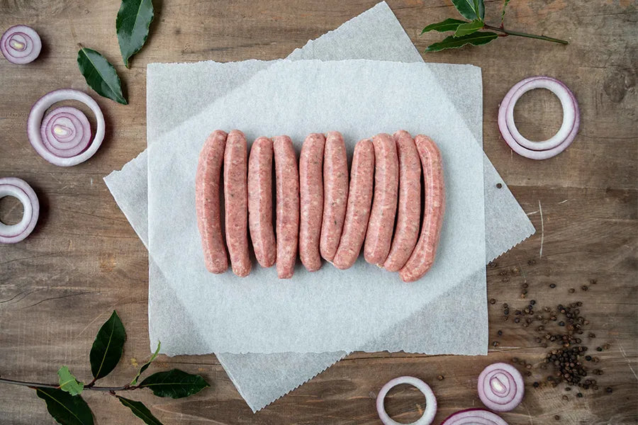 10 sausages sitting on baking paper on wooden table with onion rings around it