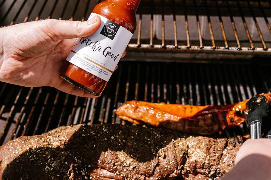 hand holding hot sauce over bbq beef meat