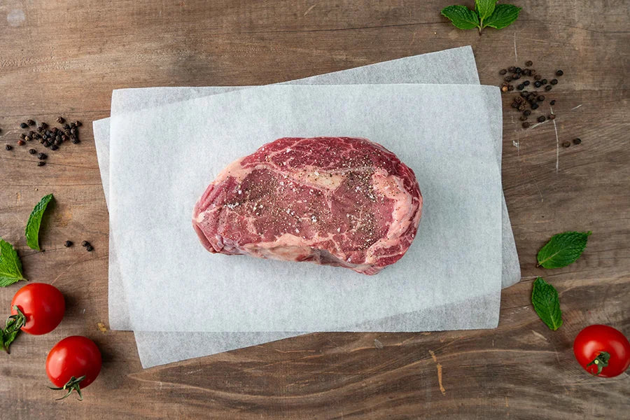 Angus Scotch fillet piece, seasoned with pepper and salt, on baking paper on wooden table