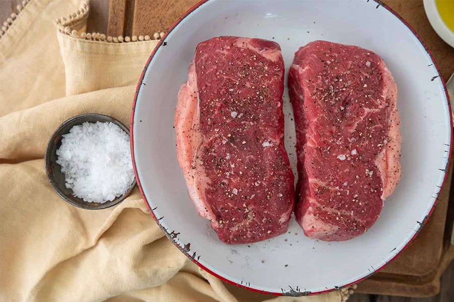 Plate with two raw sirloin steaks and small bowl of sea salt